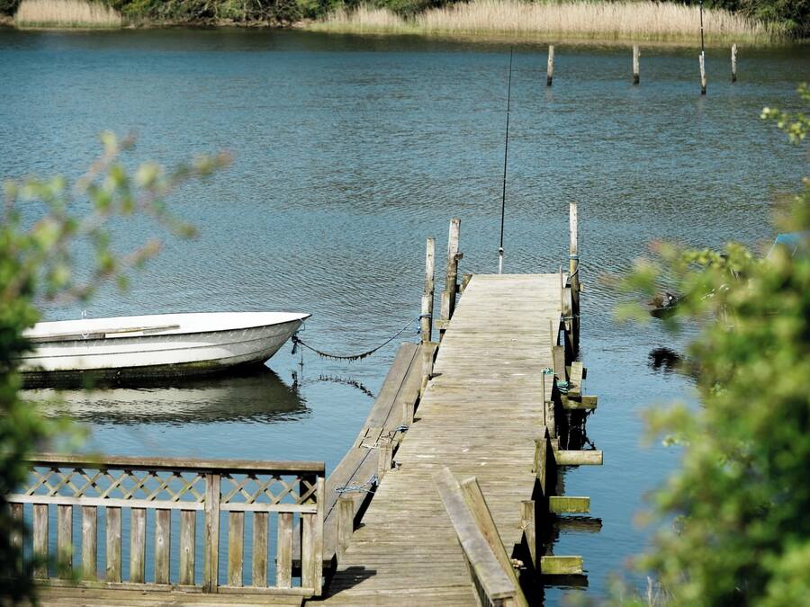 A wooden dock extending into a calm lake with a boat tied at the end.