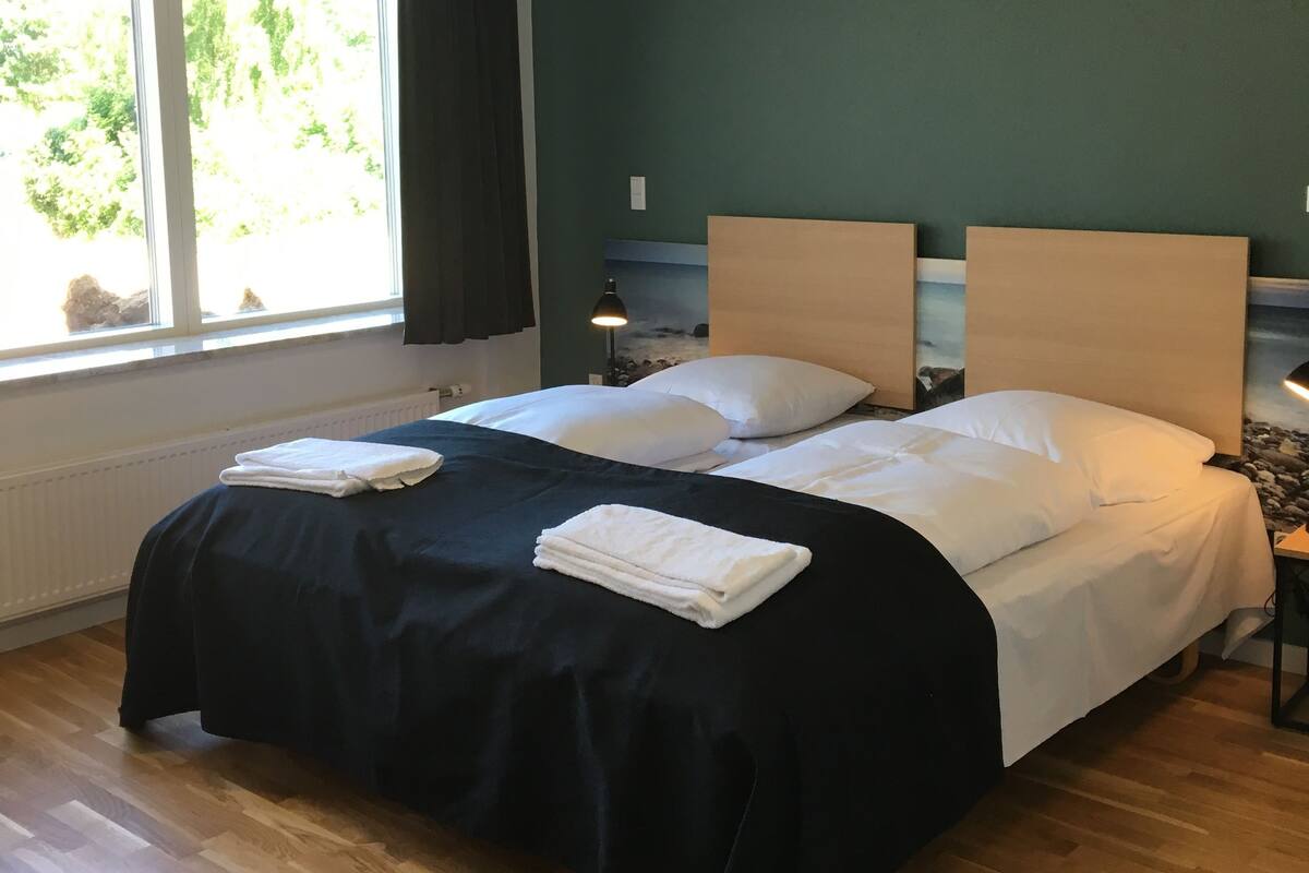 Une chambre d’hôtel avec un grand lit, une fenêtre donnant sur un espace verdoyant et un plancher en bois.