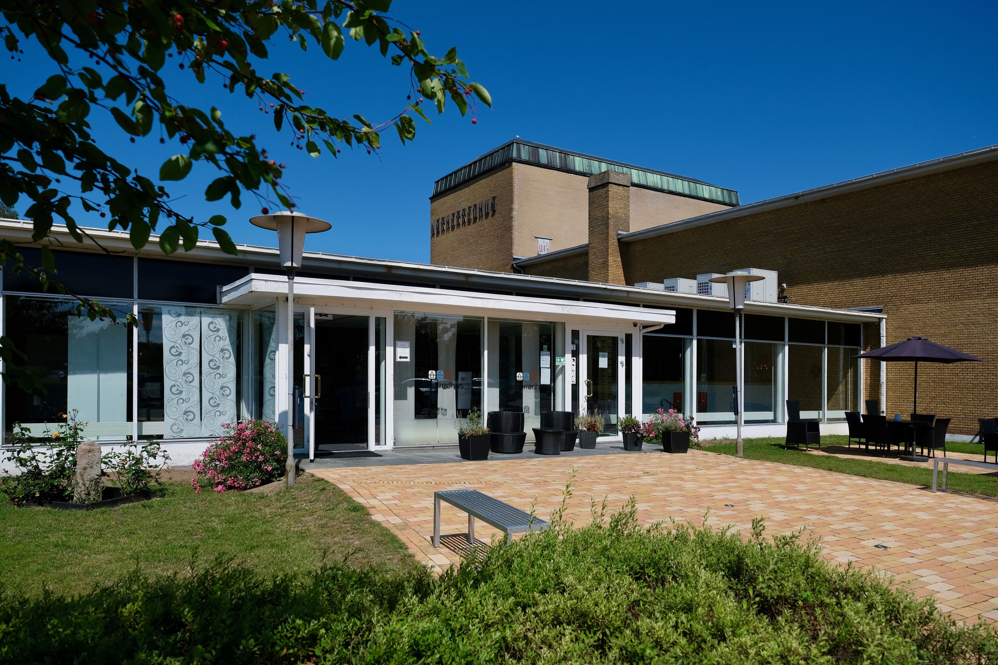 A building with a covered outdoor seating area, a brick facade, and a glass entrance.