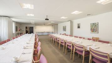 A conference room with long tables set for meetings, equipped with chairs and tables, and a projector on the ceiling.