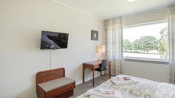 A hotel room with a bed, a desk, a chair, a television, and a window with a view of trees.
