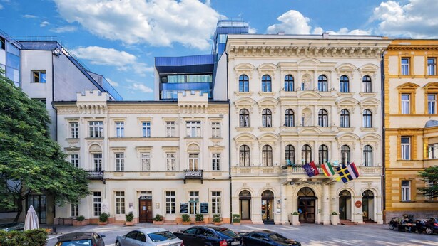 A row of historic buildings with a modern glass structure, flags, and parked cars. - Hotel President Budapest, Affiliated by Meliá (Budapest)