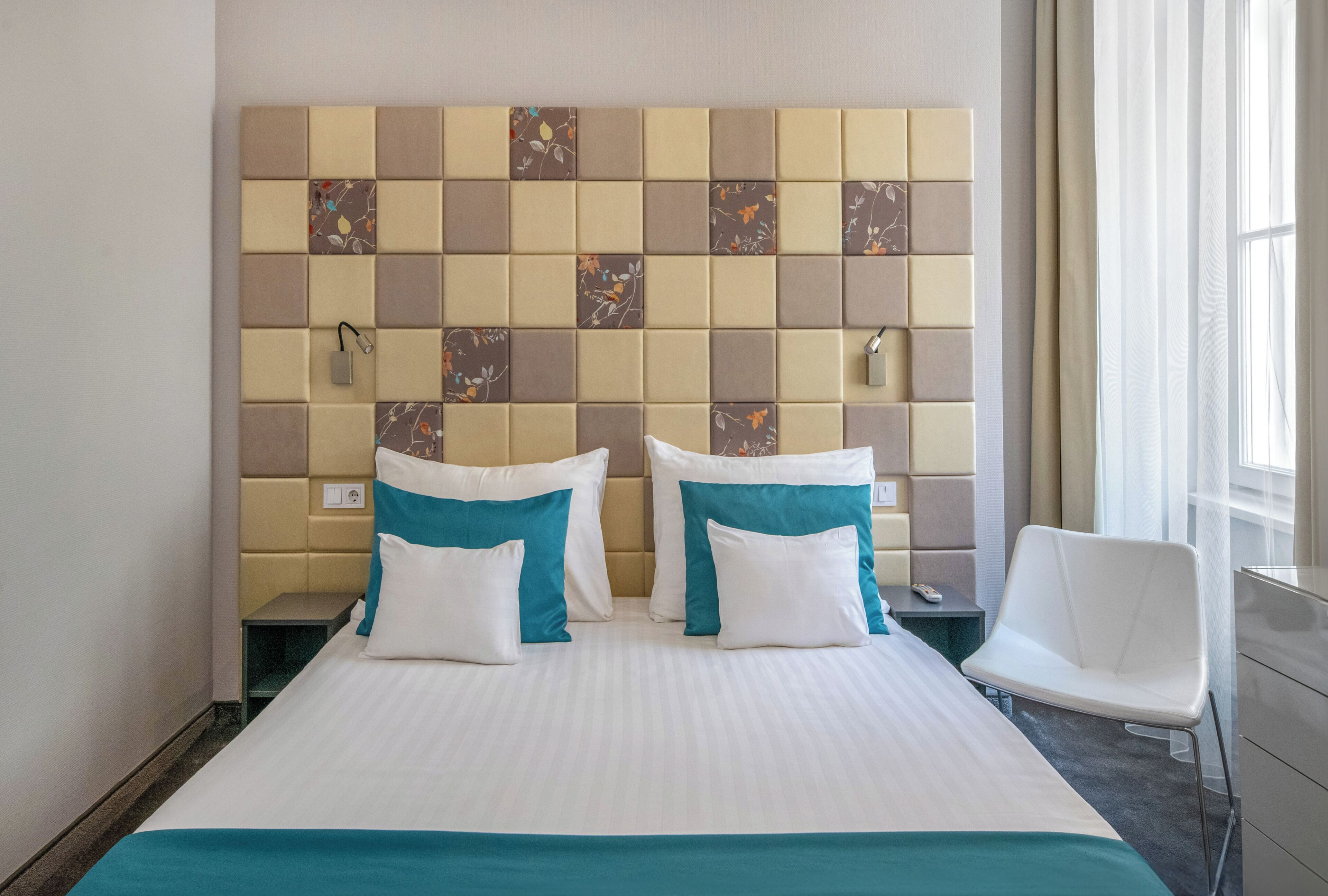 A hotel room with a large bed, two pillows, a bedside table, a chair, and a decorative wall.