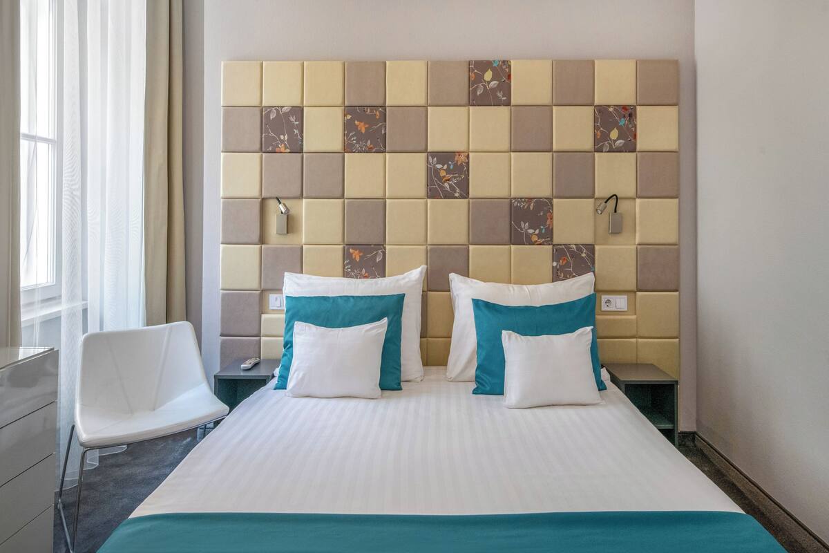 A hotel room with a bed, two bedside tables, a chair, and a headboard with a patterned design.