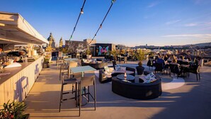 An outdoor seating area with tables and chairs, a bar, and a view of the city skyline. - Hotel President Budapest, Affiliated by Meliá (Budapest)