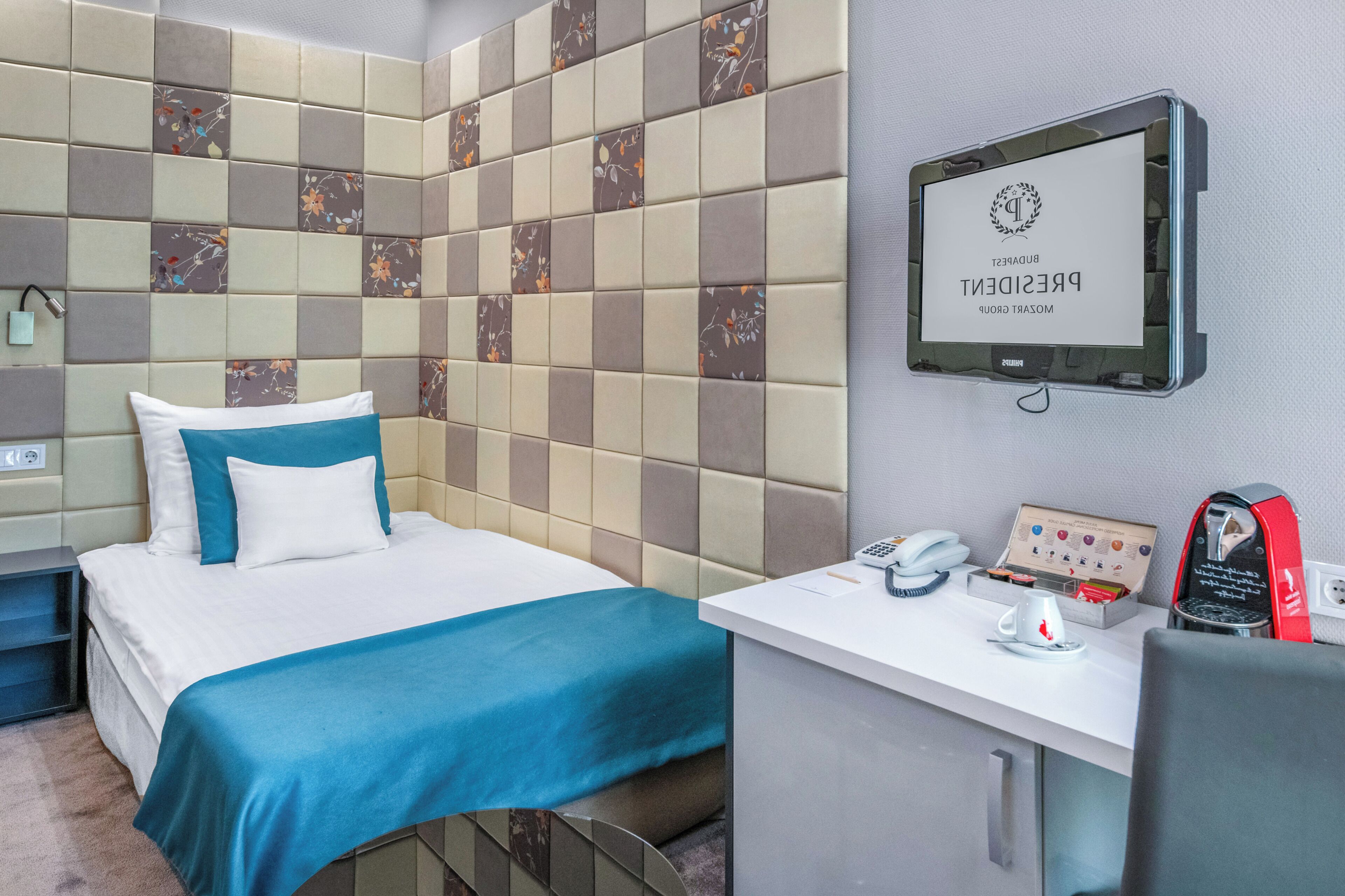 Hotelkamer met een bed, een bureau met telefoon, koffieapparaat en televisie waarop een welkomstbericht staat.
