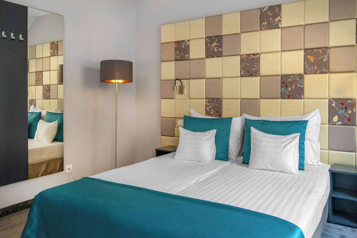 A hotel room with a large bed, a mirror, a nightstand, and a wall with a patterned design.