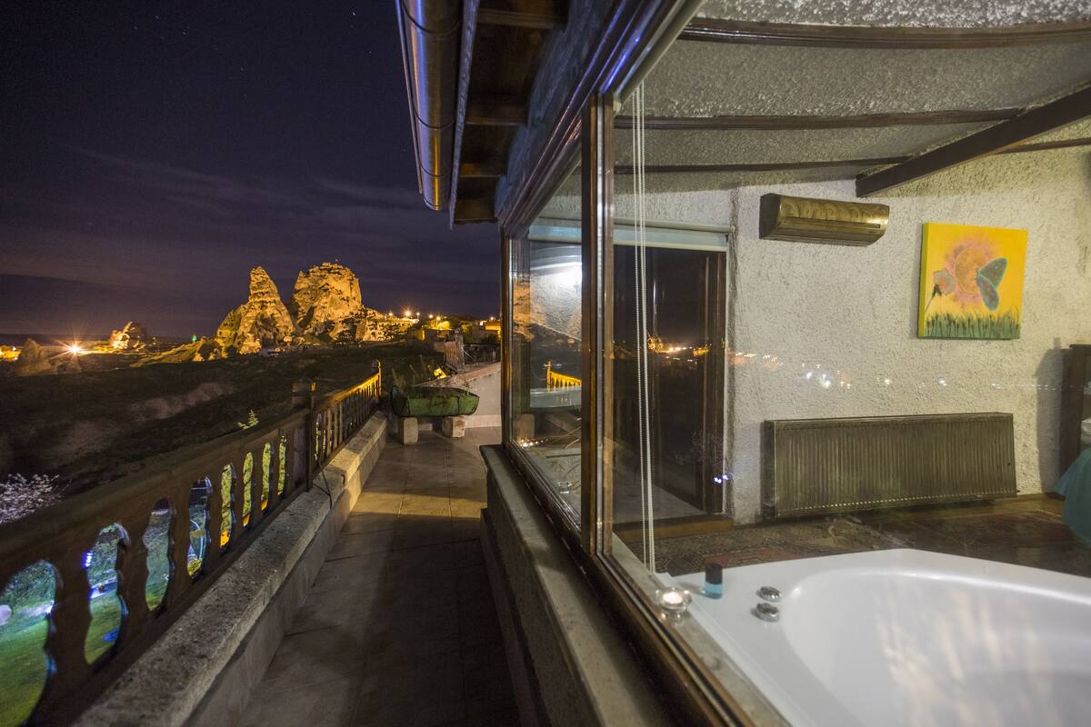 Un balcón con vista a una cadena montañosa de noche, una bañera y un cuadro en la pared.