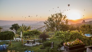 Un jardin avec des tables et des chaises, une piscine et une vue sur le coucher de soleil et les montagnes.