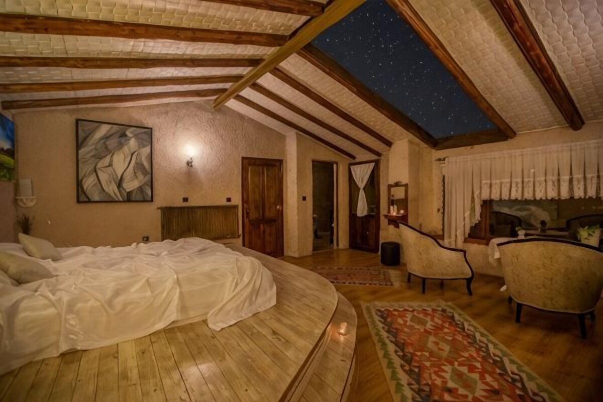 Une chambre avec un grand lit, une vue sur le ciel étoilé grâce à une lucarne, un tableau au mur et un coin salon avec des fauteuils.
