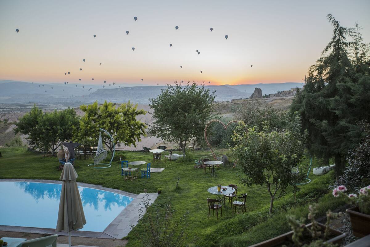 Zona de piscina con mobiliario exterior y vistas a globos aerostáticos a lo lejos.