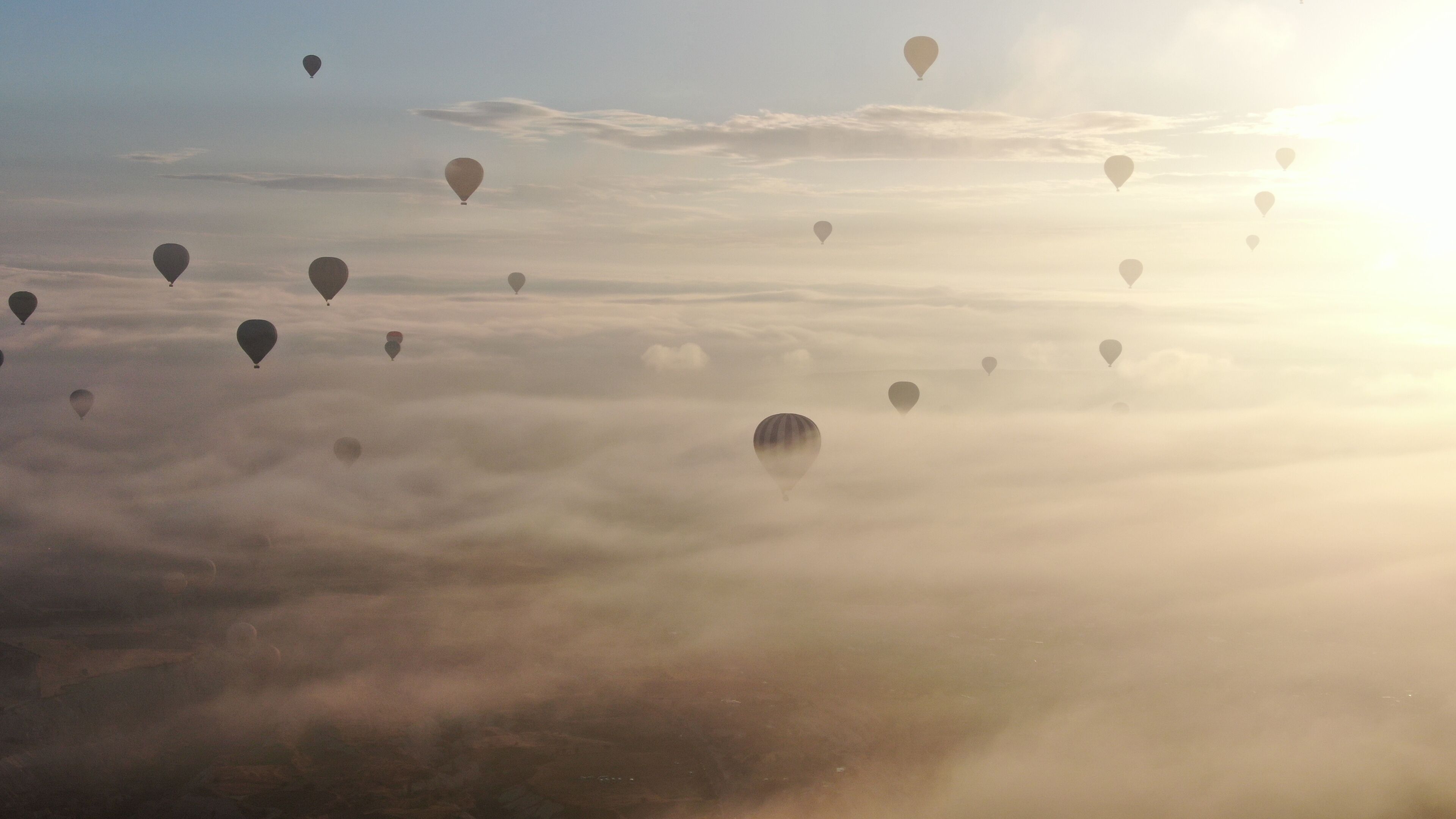 Globos aerostáticos flotando sobre un paisaje con cielo iluminado por el sol.