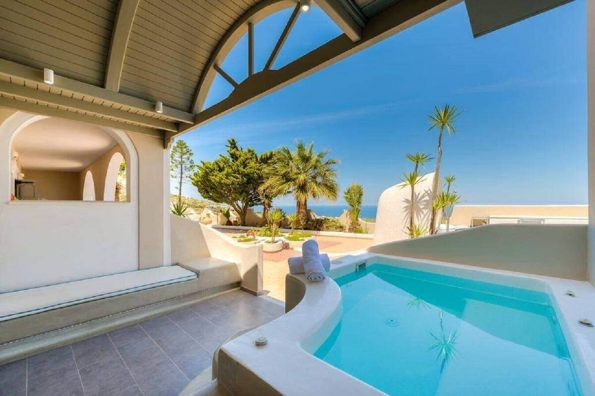 A pool area with a hot tub, a view of the sea, and a patio with plants.
