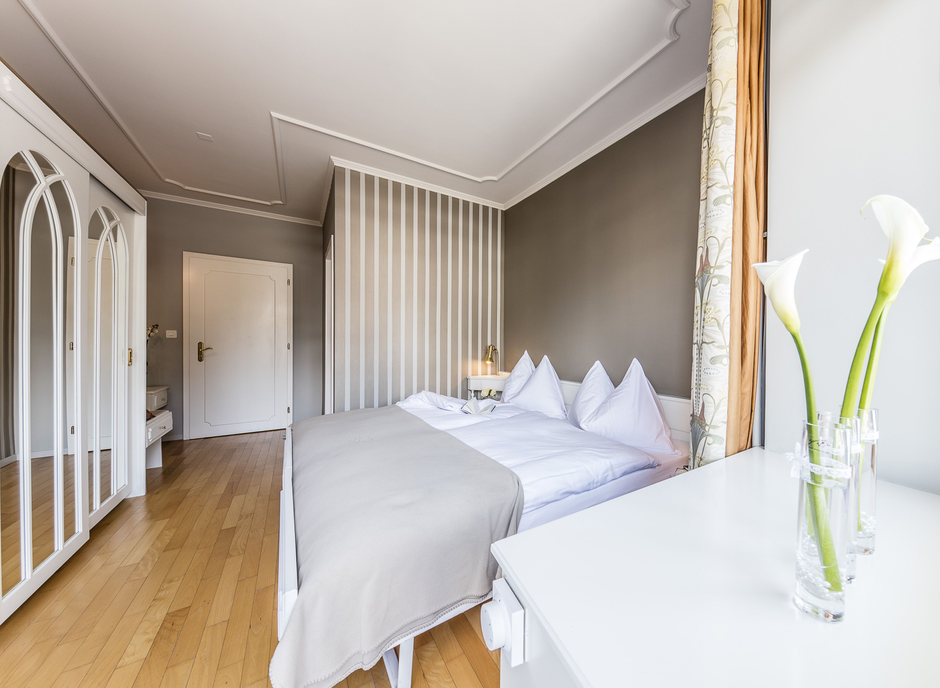 Una habitación de hotel moderna con una cama grande, una mesita de noche y un florero con flores.