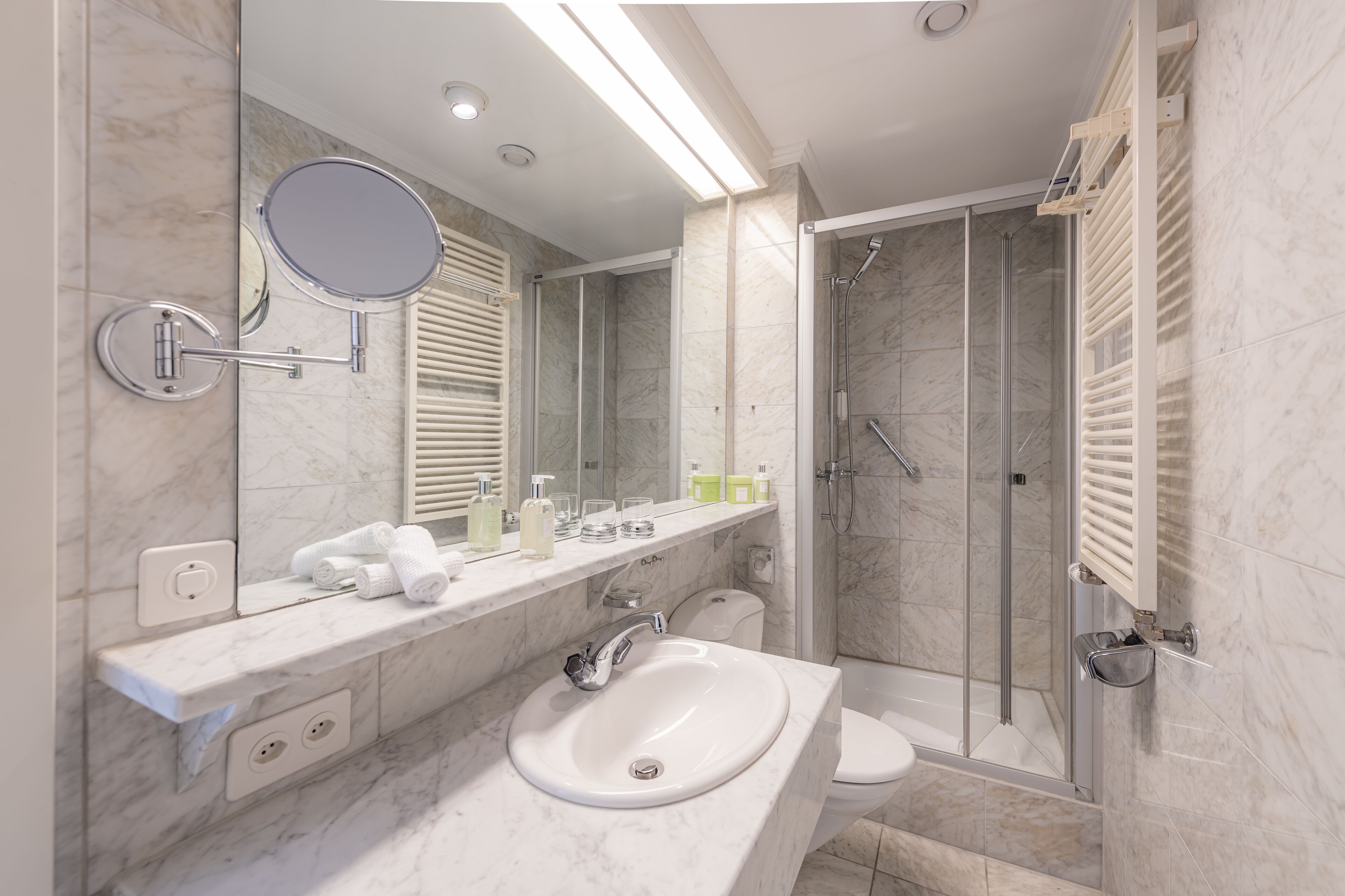 Un bagno moderno con un mobile vanitario in marmo, uno specchio grande, una cabina doccia in vetro e un water.