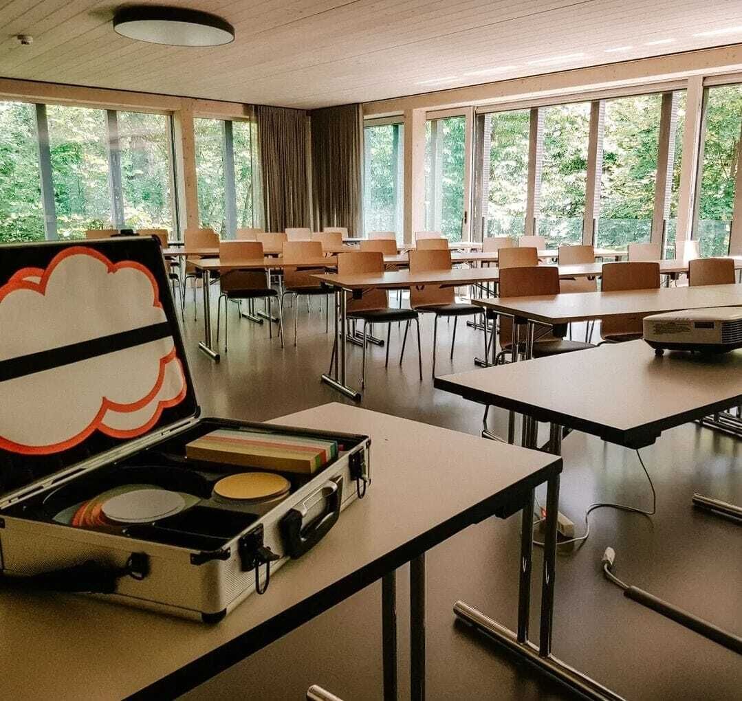 A classroom with tables, chairs, a projector, and a suitcase with a cloud design.