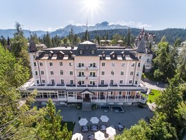 Un hotel grande de varios pisos con un patio central, rodeado de árboles y montañas.