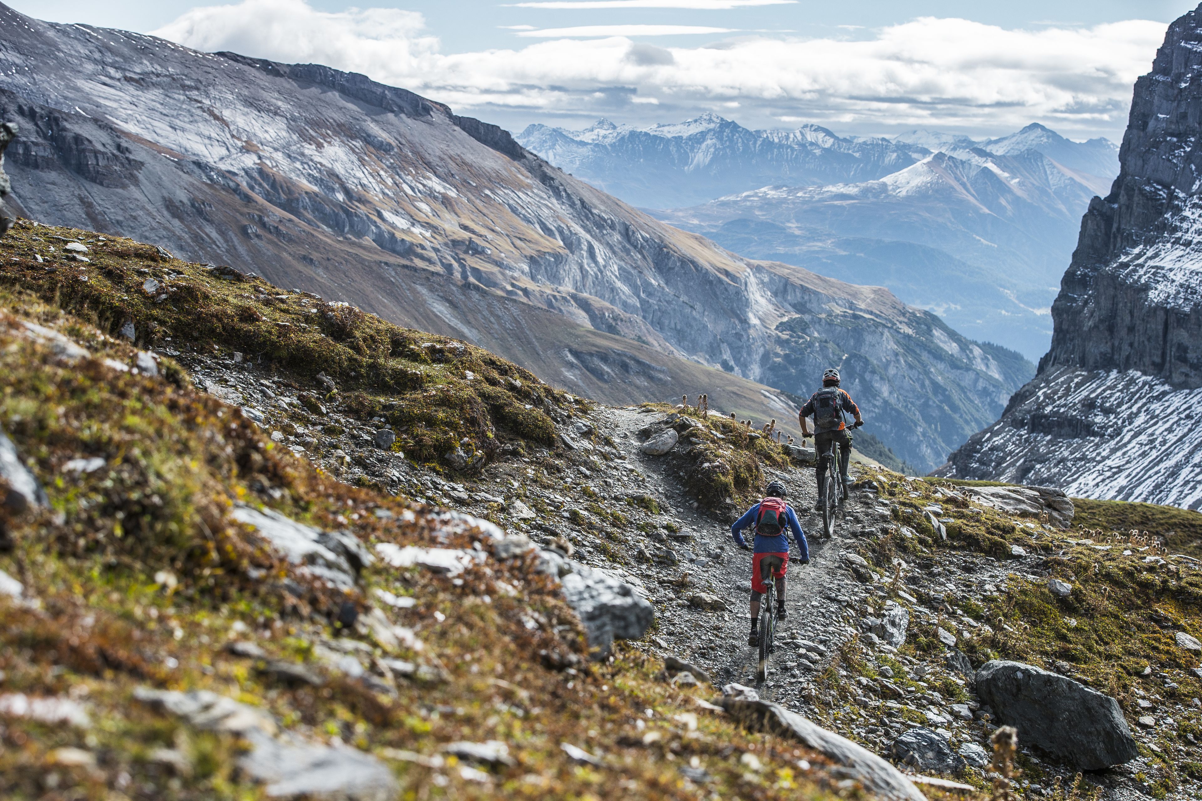 A mountain trail with rocky terrain and sparse vegetation.