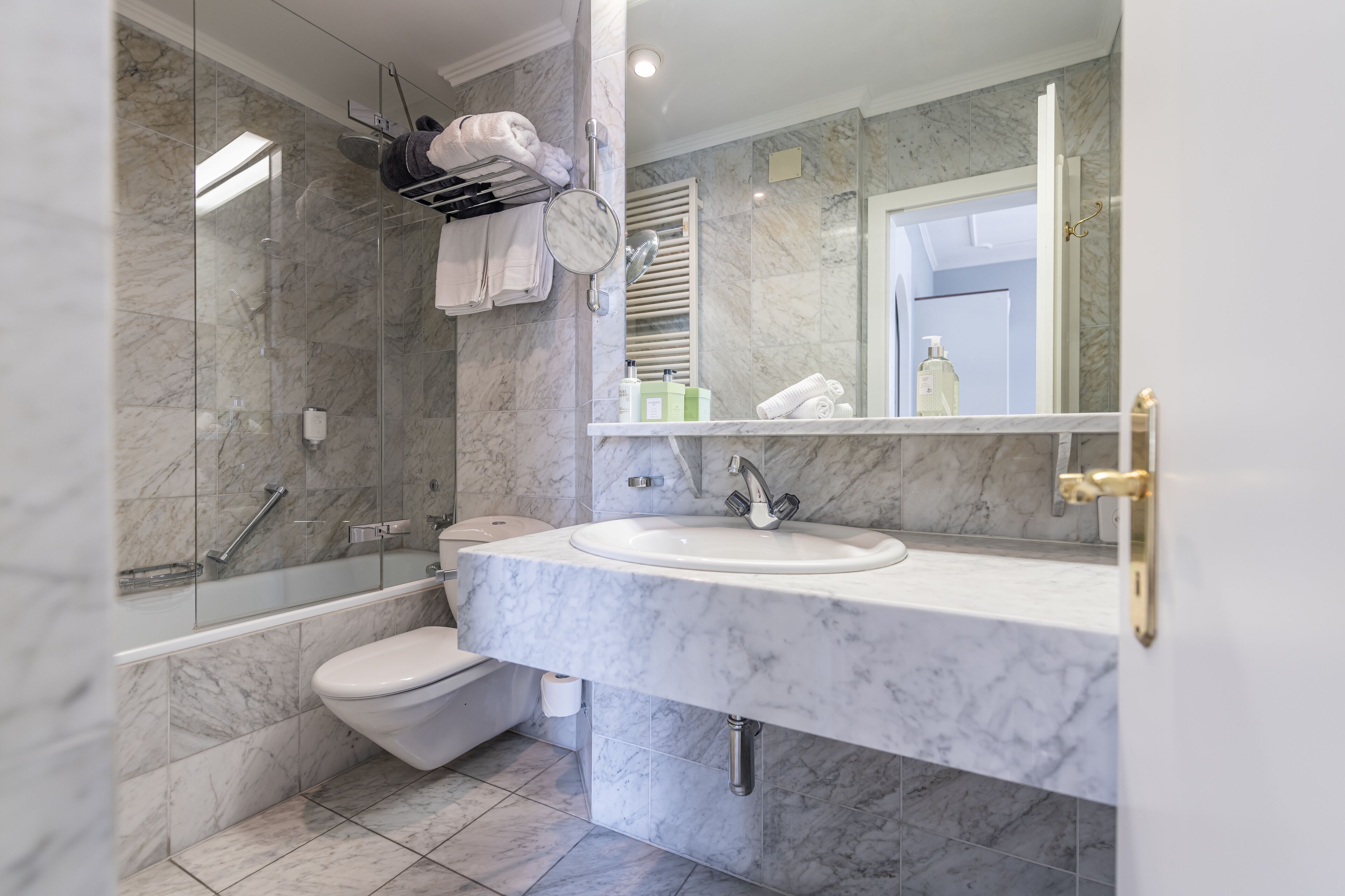 Een moderne badkamer met een marmeren wastafel, een douche met glazen wanden en een toilet.