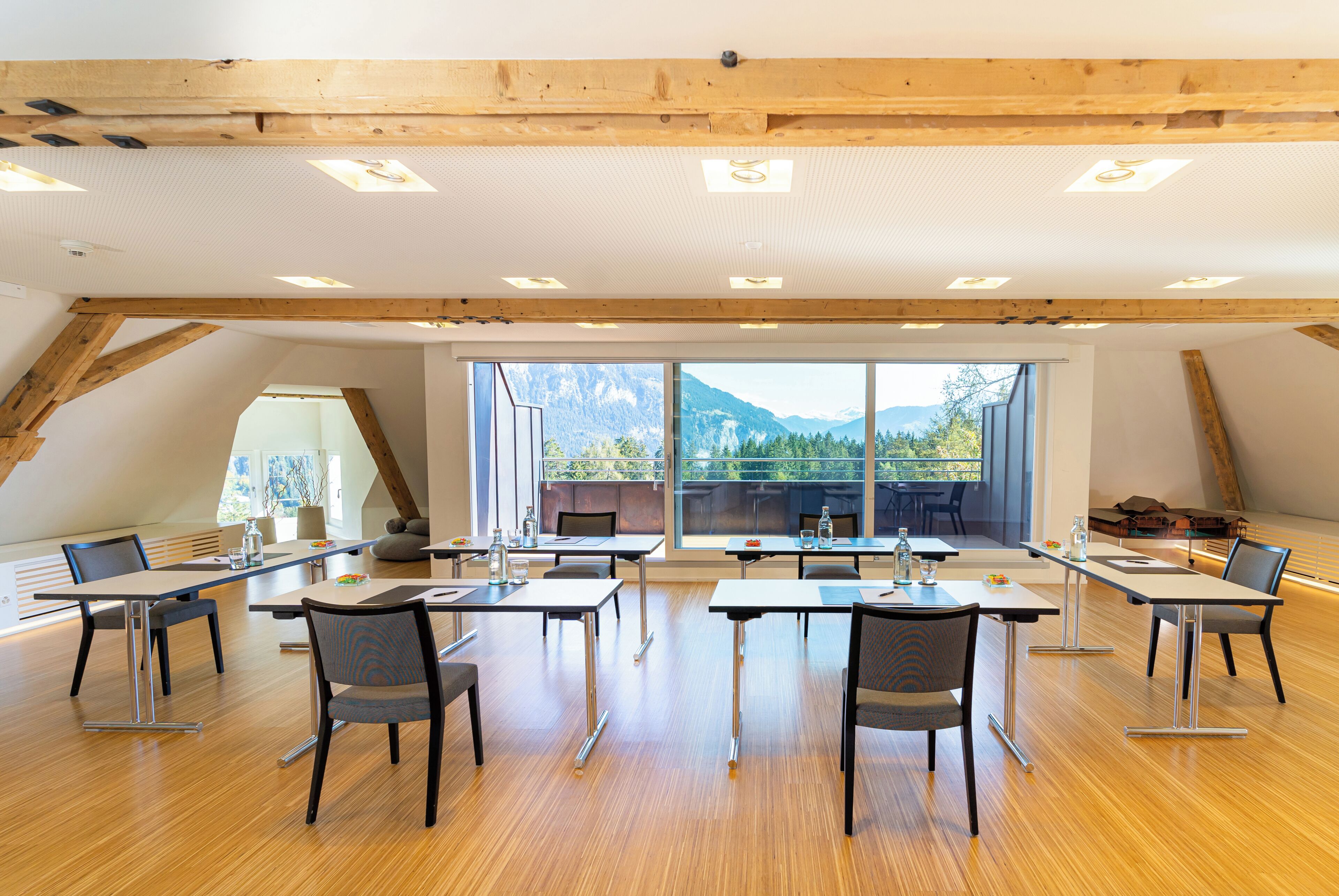 A spacious room with wooden beams, large windows, and a view of mountains.