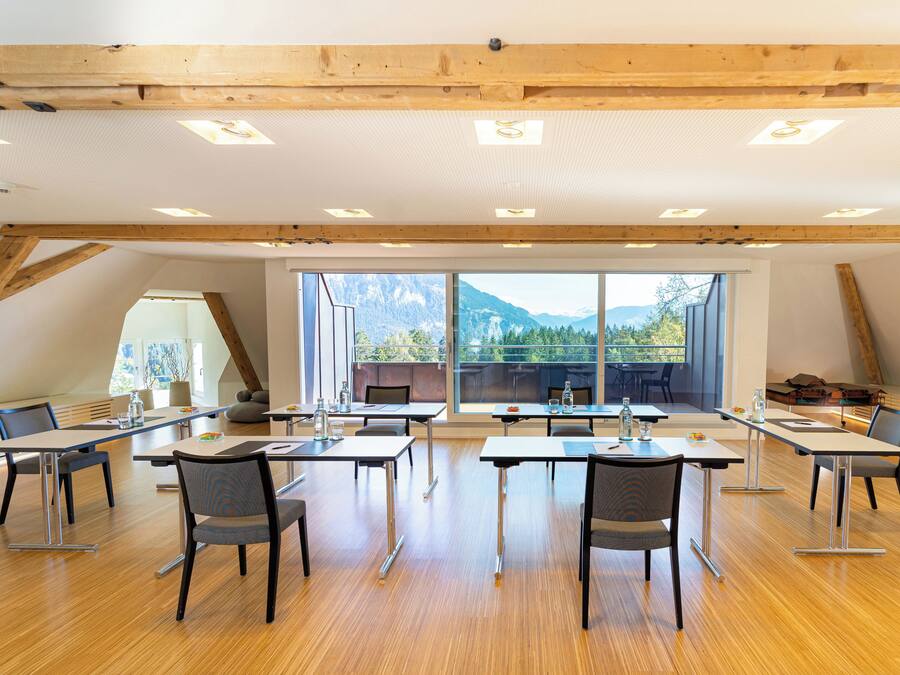 A spacious room with wooden beams, large windows, and a view of mountains.