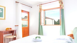 A bedroom with a bed, a desk, a chair, and a window with curtains. - Villa Mare (Hvar)