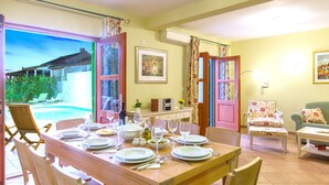 A dining area with a table set for four, a chair, a sofa, and a view of a swimming pool. - Villa Mare (Hvar)