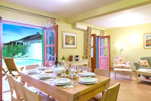 A dining area with a table set for four, a chair, a sofa, and a view of a swimming pool. - Villa Mare (Hvar)