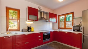 A modern kitchen with red cabinets, stainless steel appliances, and large windows. - Villa Dane (Hvar)