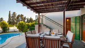 An outdoor dining area with a pool, wooden chairs, and a covered patio. - Villa Dane (Hvar)