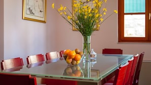 A dining table with a glass top, surrounded by red chairs, and a vase with yellow flowers and oranges. - Villa Dane (Hvar)