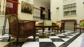 A lobby with checkered flooring, wicker furniture, a painting, and a staircase. - Hotel Doña Blanca (Seville)