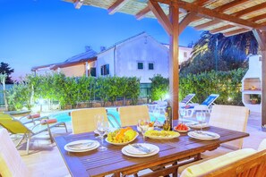 Uma área de refeições com uma mesa posta, cadeiras de exterior e uma piscina ao fundo.