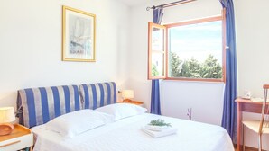 A neatly made bed with a striped headboard, a bedside table with a lamp, and a window with curtains. - Villa Cvita (Hvar)
