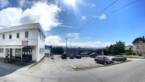 A white hotel with a 'HOTEL' sign, a covered outdoor seating area, and a parking lot with several cars. - Systra Hotel Søvik (Ålesund)