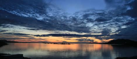 A calm body of water reflecting a sunset sky with clouds.