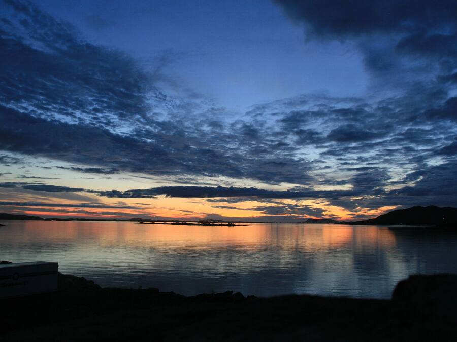 A calm body of water reflecting a sunset sky with clouds.