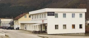 A hotel named SYSTRA with a signboard, a parking area, and a mountain backdrop.