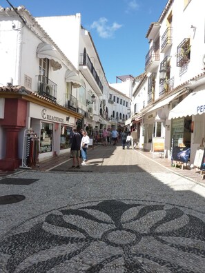 A cobblestone street lined with white buildings, some with balconies and shop fronts. - Hostal Berlin (Marbella)