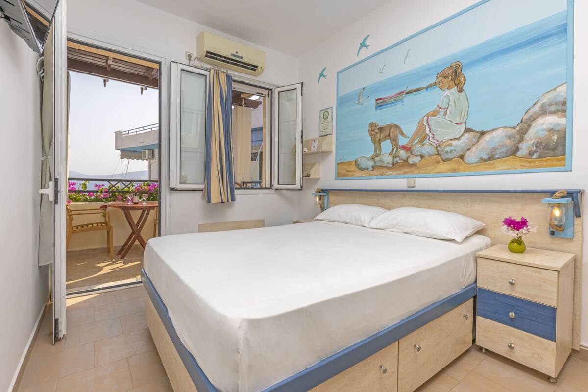 Un dormitorio con cama, mesita de noche y un cuadro de una mujer y un perro junto al mar.