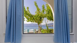 Un dormitorio con una cama, una ventana con cortinas azules y vistas a un árbol y al agua.