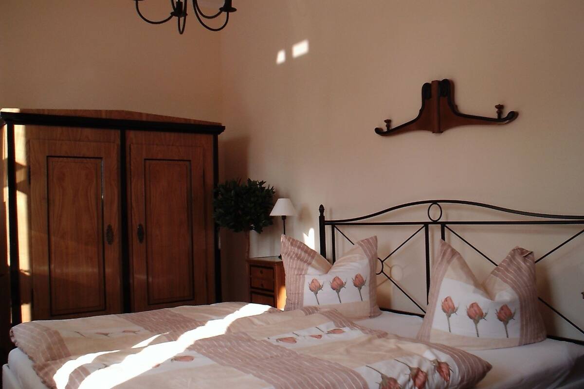 A bedroom with a bed, wooden wardrobe, and a wall-mounted hook.