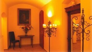 A warmly lit hallway with a chandelier, a framed painting, and a table with a vase of flowers.