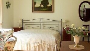 A bedroom with a bed, a painting, a mirror, and a vase with flowers.