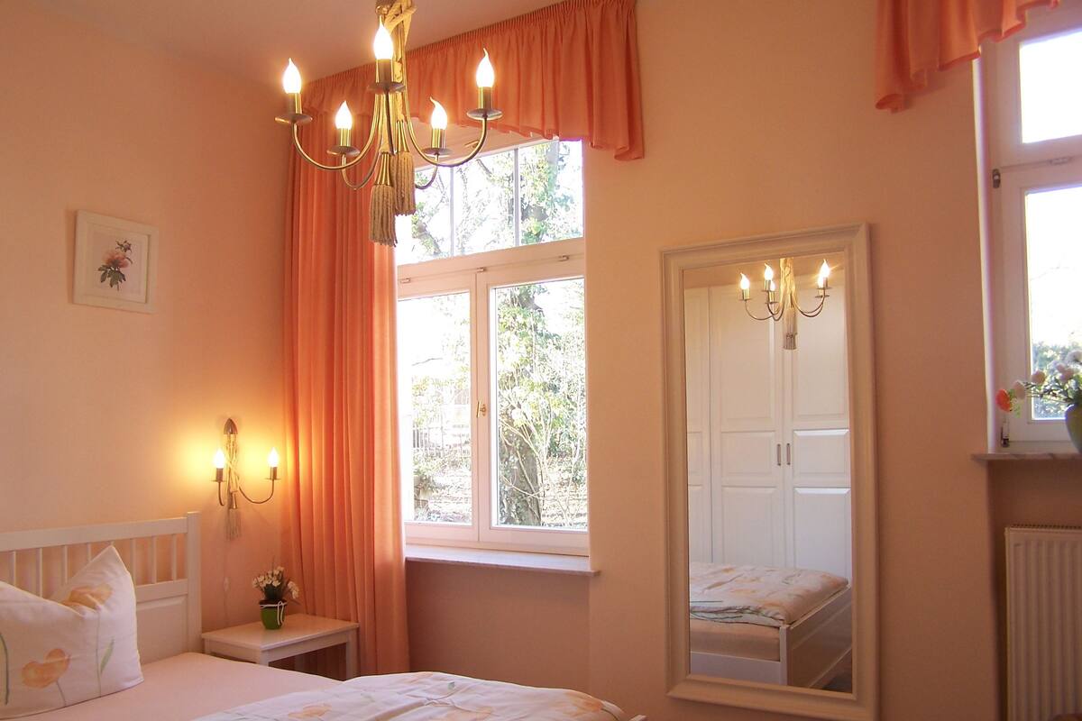 A bedroom with a bed, a nightstand, a mirror, and a window with curtains.
