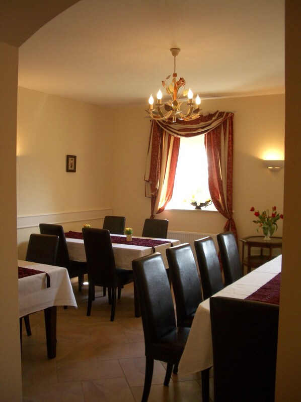 Comedor con mesas dispuestas para seis, una araña y una ventana con cortinas.