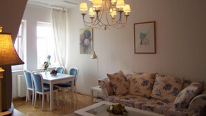 A living room with a floral sofa, a dining table with chairs, a chandelier, and a framed picture on the wall.
