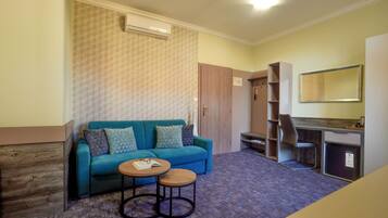 A room with a blue sofa, two small tables, a wooden cabinet, and a mirror on the wall.