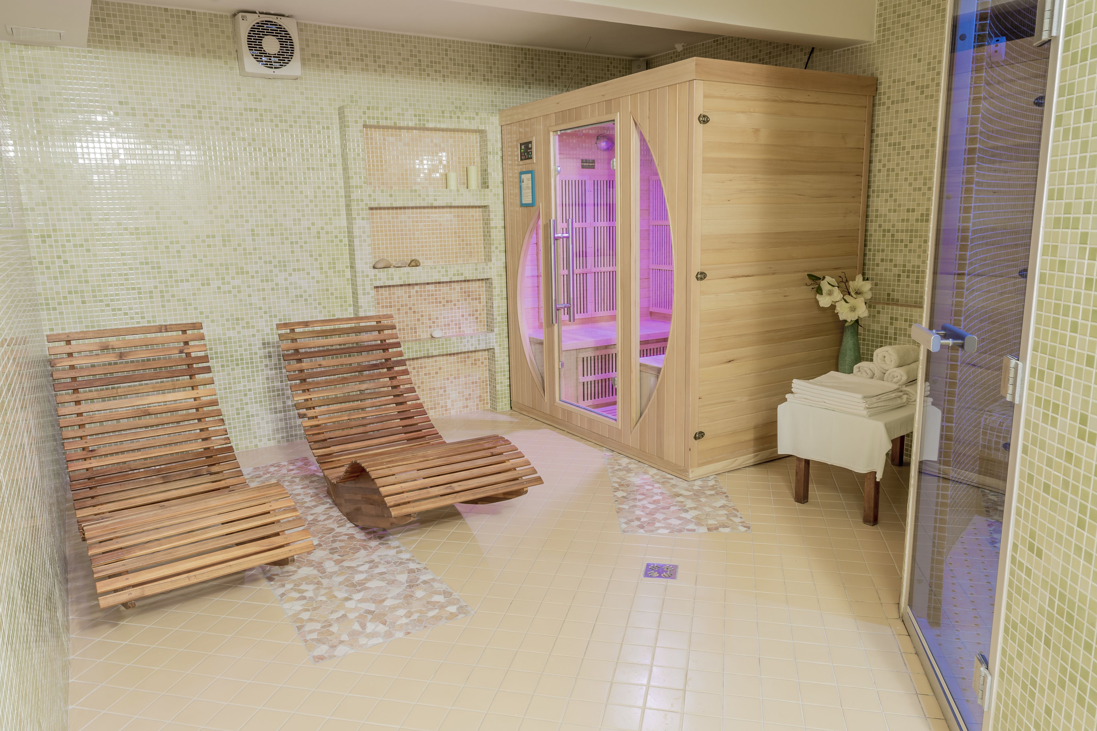 A sauna room with wooden benches, a glass-enclosed shower area, and a tiled floor.