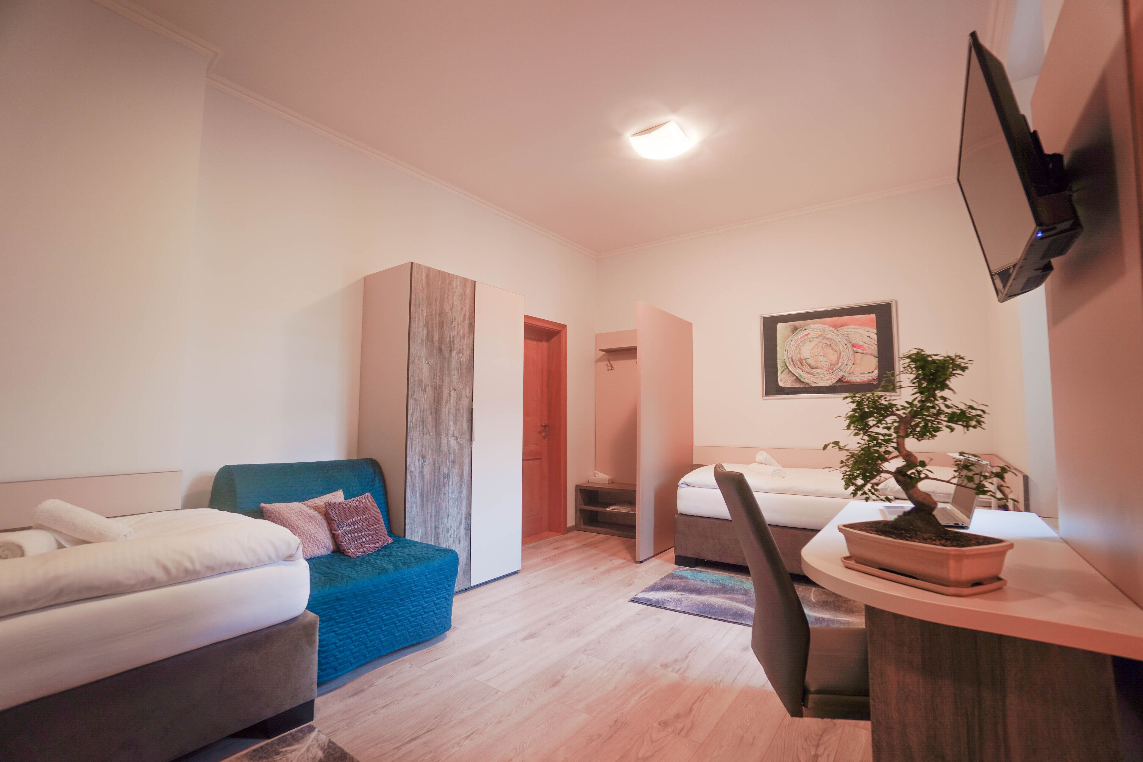 Ein modernes Hotelzimmer mit zwei Betten, einem Schreibtisch, einer Zimmerpflanze und einem an der Wand montierten Fernseher.